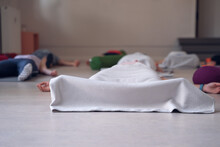 People Lying On The Floor, With Their Legs And Feet Covered By A Blanket, While Meditating, At The End Of A Yoga Class.
