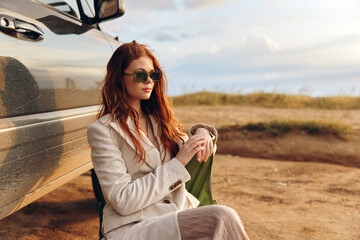 Wall Mural - beautiful woman sitting on a chair in a field wearing dark glasses near the car endless field