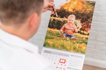 Wall Mural - man holds a calendar with a photo of a child. printed products.