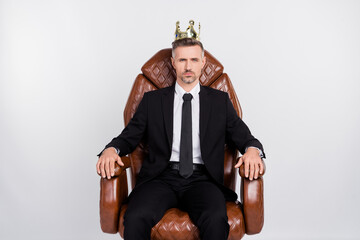 Poster - Photo of serious handsome young agent wear black jacket gold crown sitting comfort leather armchair isolated grey color background