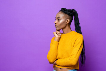 Young African-American woman thinking with hand on chin in isolated purple color studio background