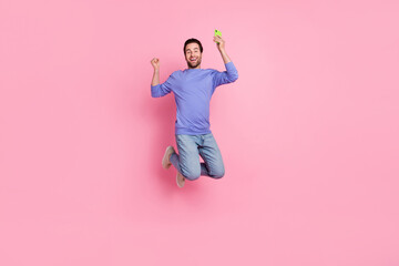 Poster - Full length photo of brunet cool millennial guy jump hold telephone wear blue pullover jeans sneakers isolated on pink background