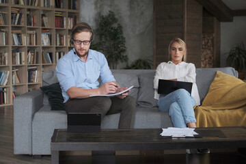 Modern business man and woman freelancer working together use laptop and headset at home office. Couple partners remotely studying enjoying distance education taking paper notes discussing planning