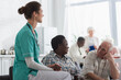 © LIGHTFIELD STUDIOS - Young nurse holding hand of african american patient with tea in nursing home