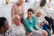 © LIGHTFIELD STUDIOS - Senior man holding digital tablet near nurse and interracial friends in nursing home