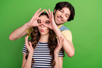 Canvas Print - Photo of young crazy couple happy positive smile make fingers binoculars glasses isolated over green color background