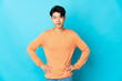 Young Chinese man isolated on blue background posing with arms at hip and smiling
