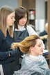 © okskukuruza - Two female hairstylists prepare long hair of a young woman making curls hairstyle in a beauty salon