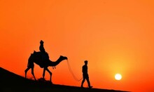 Silhouette Man Riding Camel Against Orange Sky