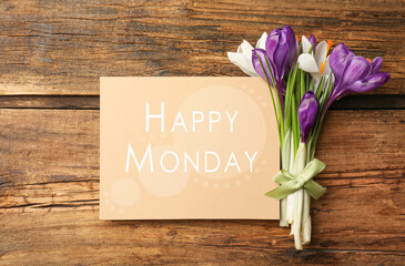 Beautiful spring crocus flowers and card with phrase Happy Monday on wooden table, flat lay
