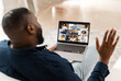 © Vadim Pastuh - Morning meeting with diverse colleagues. African-American guy using computer app for virtual communication with a group of international people, making video call, greeting, staying at home, back view