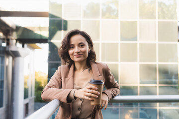 Wall Mural - positive woman with takeaway drink looking at camera on balcony outdoors