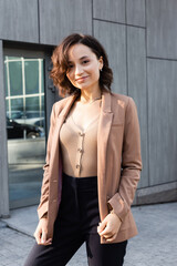 Wall Mural - brunette woman in beige blazer smiling at camera while standing outdoors