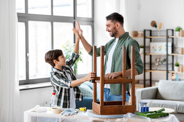 family, diy and home improvement concept - happy smiling father and son restoring old table and making high five gesture at home