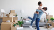 © Prostock-studio - Glad millennial african american husband hugs and lifts his wife in new apartment around cardboard boxes and things