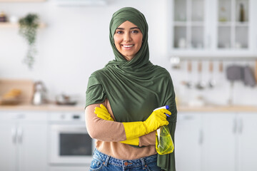 Wall Mural - Cheerful young islamic housewife holding spray bottle posing at camera