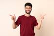 © luismolinero - Young Moroccan man isolated on beige background pointing finger to the laterals and happy