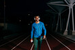© ADDICTIVE STOCK - Athlete listening music and walking on the running track at night