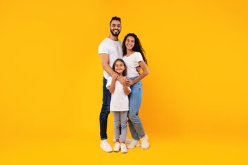 Wall Mural - Full-Length Shot Of Middle-Eastern Family Hugging Standing On Yellow Background