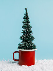 Wall Mural - Creative Christmas composition with red tea cup, snow and pine tree on pastel blue background. Minimal Xmas eve or New Year celebration concept. Elegant winter holidays scene. Cute mug of hot drink.