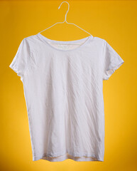 Wall Mural - white cotton crumpled t-shirt hanging on a hanger on a yellow background, summer clothes