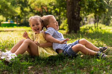 Two happy smiling cheerful toddler preschool twins siblings children brother sister boy girl sitting together on grass lawn in park in sunny hot summer weather. childhood, friendship, family concept