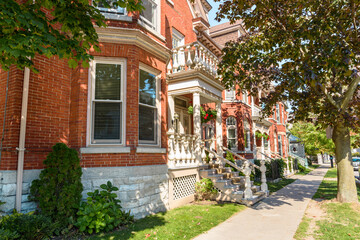 Row of traditional red brick townhouses along a tree lined pavement on a sunny autumn day