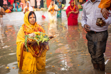 women performing chhath festival, standing in river water with offering prasad for god in their hand