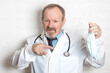 © Елена Белоусова - A doctor holds a mask in one hand, and points at it with the other, this is a recommendation to wear masks to protect yourself from Covid-19