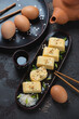 Tamagoyaki or japanese rolled omelette over brown stone background, vertical shot, selective focus