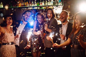 Young  friends celebrate new year and holding bengal lights and glasses with drink.Winter holidays.