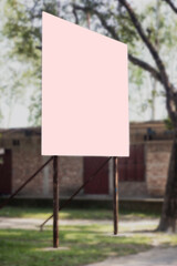 a big pink white signboard attaches two iron poles under a big tree and the background blur behind i