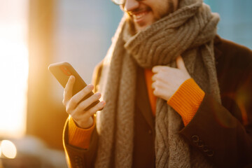 Оnline communication. Young man in winter clothes walking on the street and looking his phone and sending message. Business concept