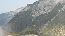 A Yellow Rescue Helicopter Flying Away In Front Of An Alpine Panorama.