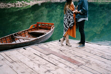 Pregnant Woman And Man Stand On The Pier By The Lake Near A Moored Boat. Close-up