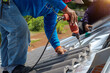 © ปราณี จิรกิจเดโชกุล - Roof repair, worker with white gloves replacing gray tiles or shingles on house with blue sky as background and copy space, Roofing - construction worker standing on a roof covering it with tiles.