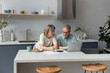 © fizkes - Serious older 60s married couple discussing budget, income, expenses, calculating money, counting insurance fees at calculator, doing paperwork together. paying bills, taxes, using laptop in kitchen