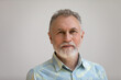 © fizkes - Serious older man in casual with beard head shot portrait. Grey haired retiree, pensioner posing, standing isolated against white wall background. Close up male portrait, elderly age concept