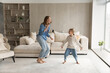 © fizkes - Happy emotional young mother or babysitter dancing to disco music barefoot with laughing adorable little child daughter in light living room, having fun laughing enjoying domestic hobby activity.
