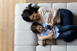 © fizkes - Woman and little 6s son lying on cozy sofa with smartphone, above view. Family spend leisure at home using modern tech usage, play games, buy goods, enjoy new cool amusing mobile app for kids concept