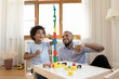 © fizkes - Excited Black little son and happy dad building high toy tower together, playing with construction blocks for kids, completing model, enjoying family playtime, game, entertainment at home. Fatherhood