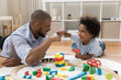 © fizkes - Proud dad and happy little son bumping fists over toy blocks and railway model on heating floor. Father giving praise to kid, expressing approval, enjoying friendship, fatherhood, playtime