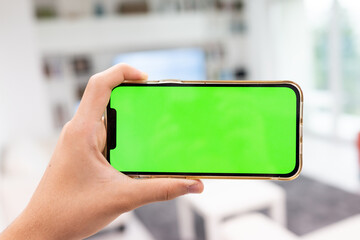 Hand in modern living room via smart home on mobile phone with blank green screen. High quality photo