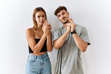 Wall Mural - Young beautiful couple standing together over isolated background holding symbolic gun with hand gesture, playing killing shooting weapons, angry face