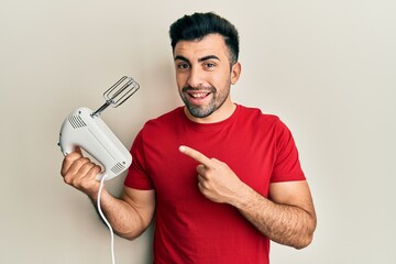 Young hispanic man holding food processor mixer machine smiling happy pointing with hand and finger