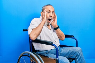 Poster - Handsome senior man with beard sitting on wheelchair afraid and shocked, surprise and amazed expression with hands on face