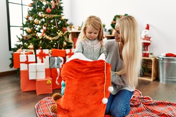 Wall Mural - Mother and daughter holding gifts on christmas bag sitting on the floor at home