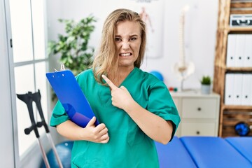 Sticker - Young caucasian woman working at pain recovery clinic pointing aside worried and nervous with forefinger, concerned and surprised expression