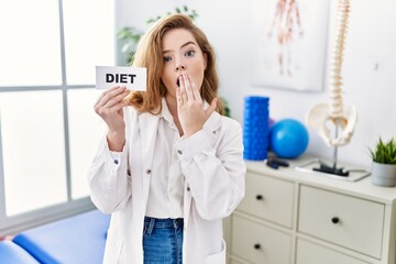 Wall Mural - Young caucasian woman working at rehabilitation clinic holding diet banner covering mouth with hand, shocked and afraid for mistake. surprised expression