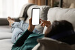 © fizkes - Female using phone. Over shoulder view of young woman lying on sofa hold smartphone with blank empty screen. Template for web app chat interface online advertisement mobile game social network profile